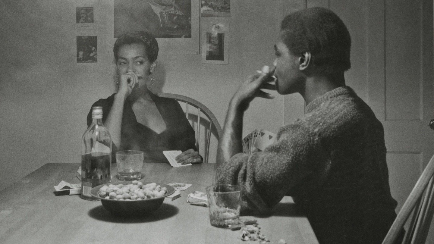 Carrie Mae Weems, Kitchen Table Series: người phụ nữ ngồi ở chiếc bàn bếp gỗ dưới ngọn đèn treo, ảnh đen trắng