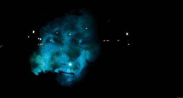 Tony Oursler, The Influence Machine: faces projected onto smoke and trees in a park at night